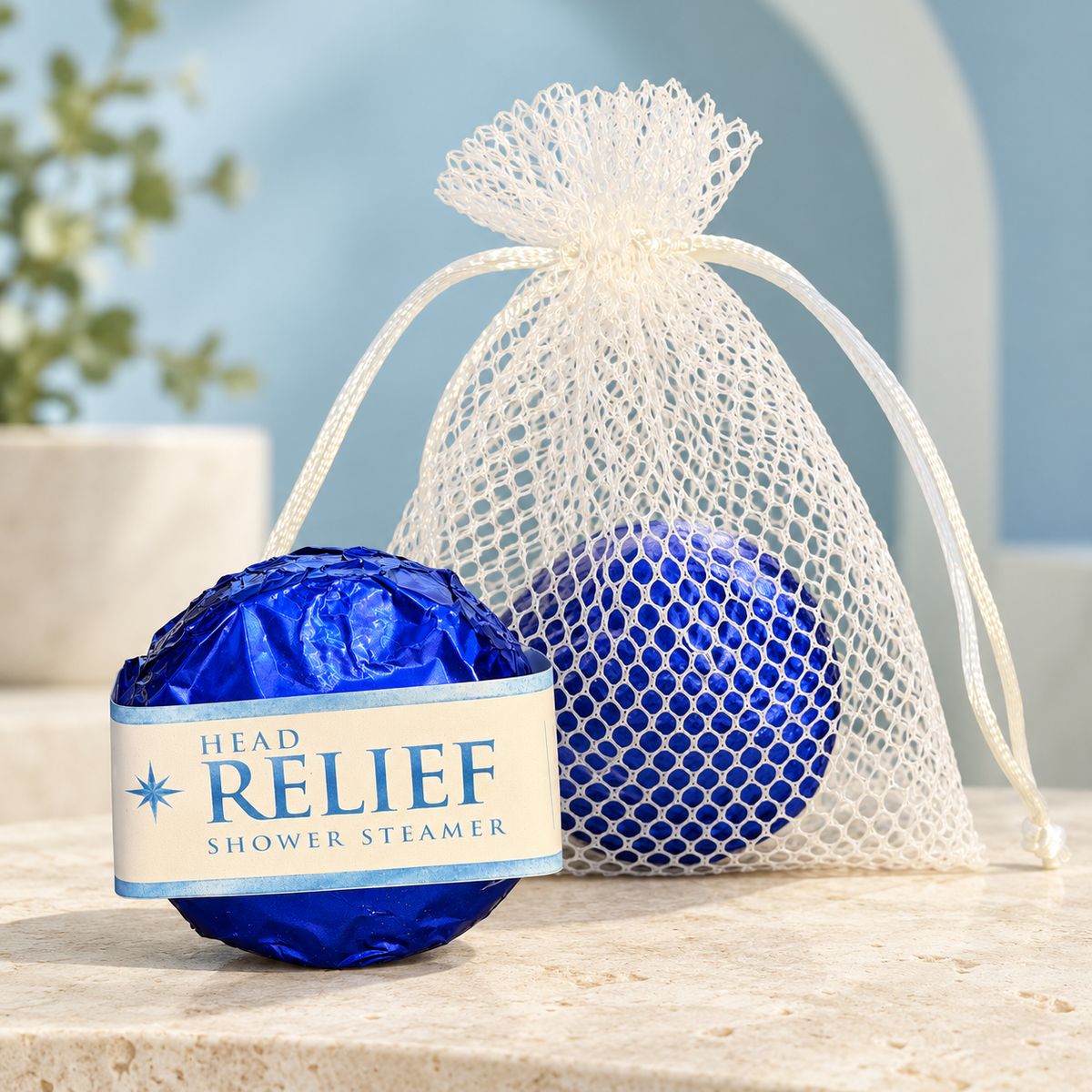 LIT Apothecary HEAD RELIEF shower steamer wrapped in blue foil beside a white mesh pouch holding another steamer, displayed on pale stone against a soft blue spa background.