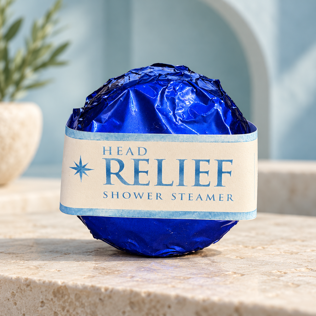 LIT Apothecary HEAD RELIEF shower steamer wrapped in blue foil with a cream and blue label, displayed on pale stone against a soft blue spa background.