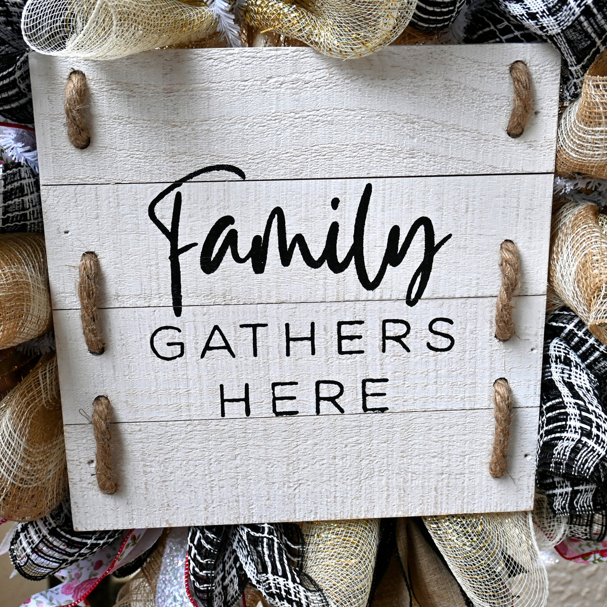 Close-up of Family Gathers Here wooden sign featured on a warm fall wreath with layered ribbon accents.