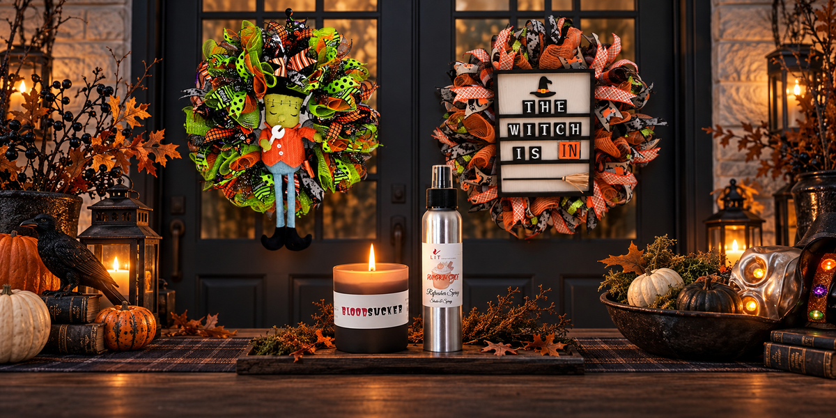A styled autumn porch scene with two decorative wreaths hanging on dark front doors, a lit candle in a white jar labeled BloodSucker, and a silver bottle with a black cap in the foreground. Pumpkins, lanterns, fall leaves, and warm string lights create a cozy Halloween atmosphere.