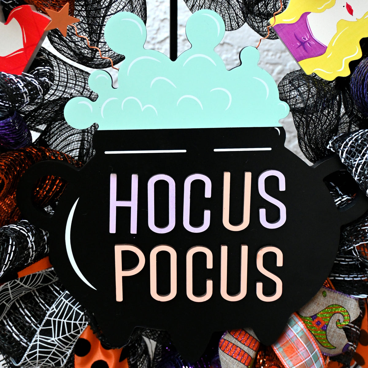 Close-up of the cauldron centerpiece on a Hocus Pocus Halloween wreath with purple, orange, black and white accents.
