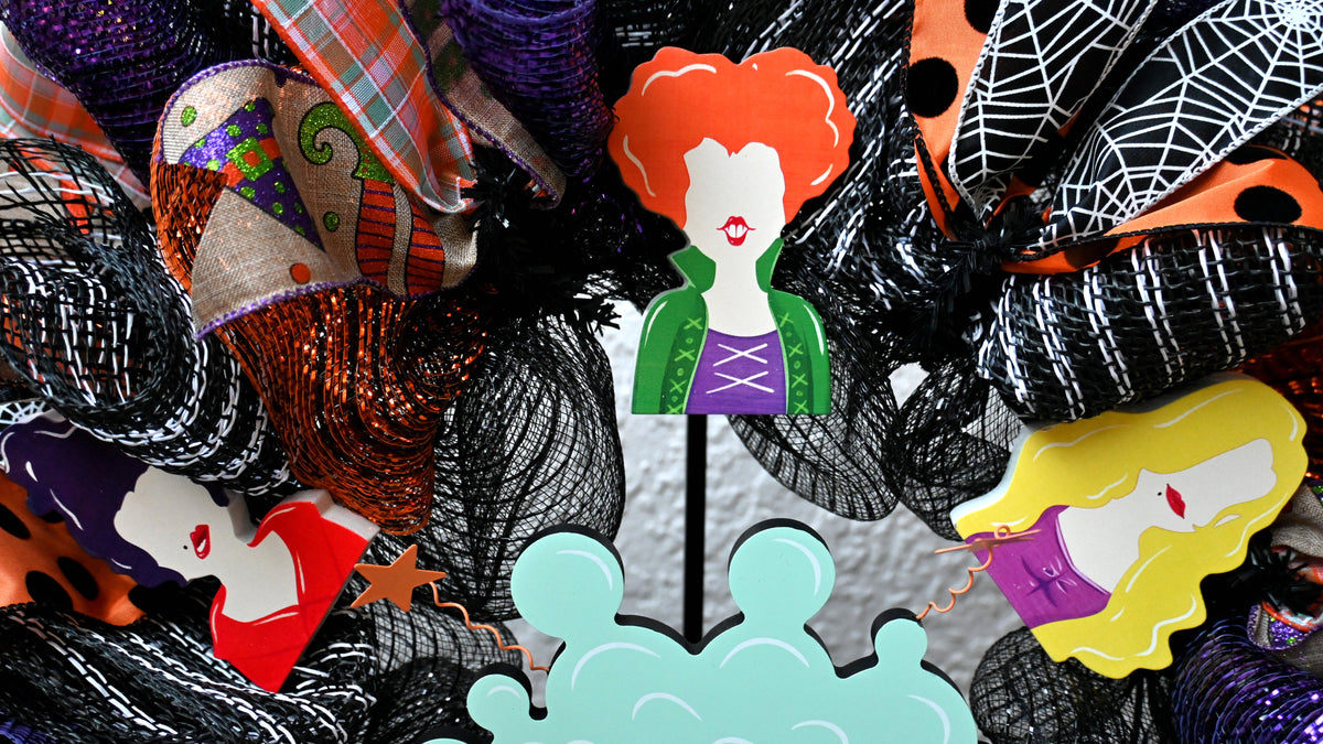 Close-up of three witch decorations and layered Halloween ribbons on a Hocus Pocus wreath.
