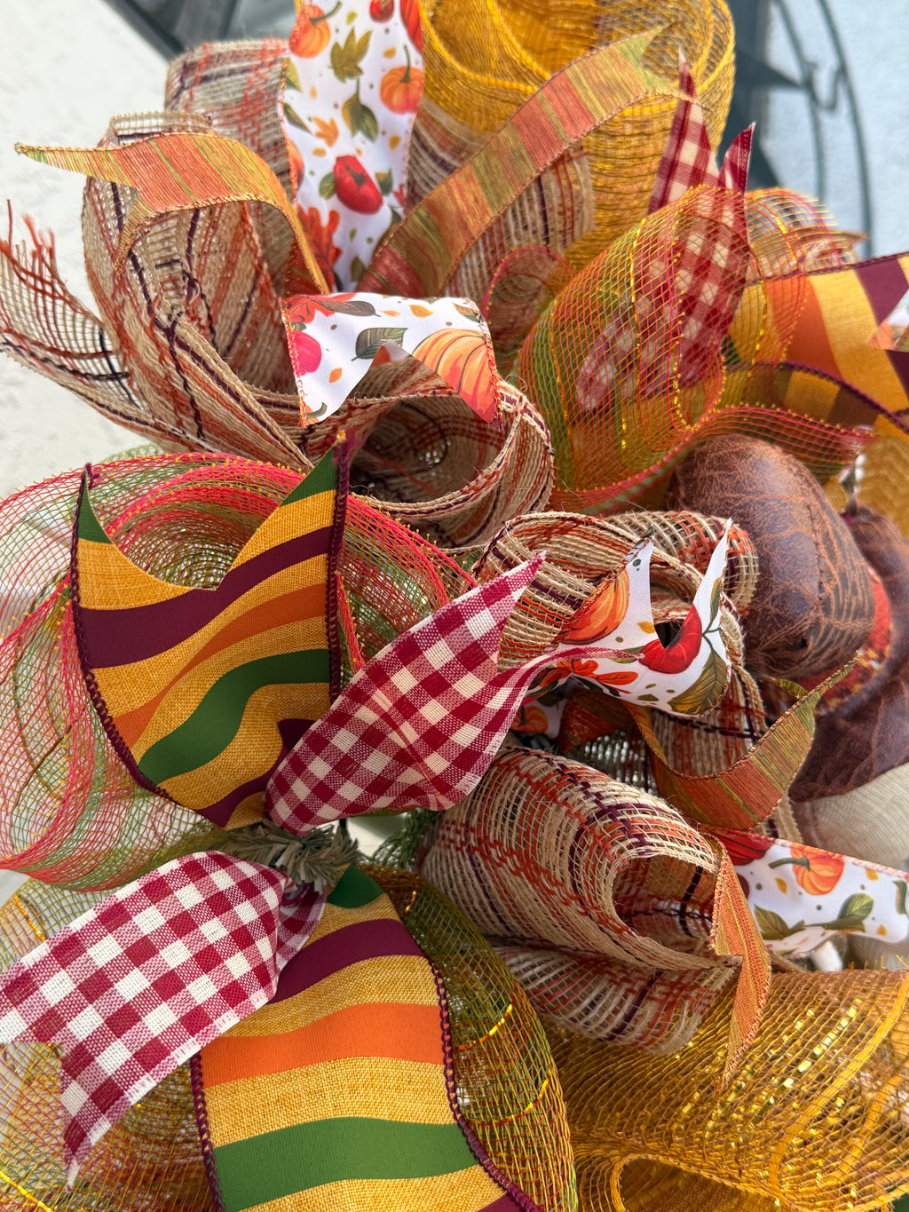 Detail of pumpkin-and-leaf print ribbon, burgundy gingham, autumn stripes, and layered deco mesh on the Thanksgiving wreath