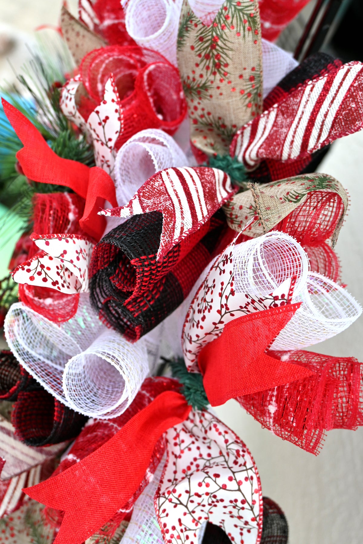 Close-up of Joy Christmas wreath ribbons with holly greenery, peppermint stripes, cranberry sprigs and woven red accents.