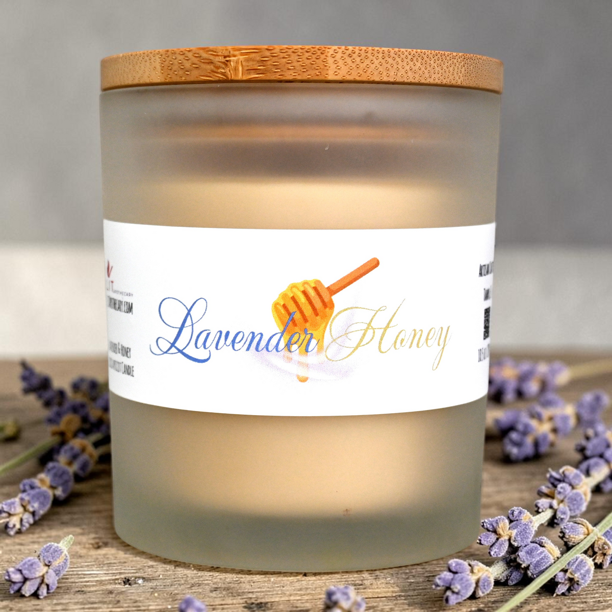 Candle labeled 'Lavender Honey' with a wooden lid on a wooden surface with lavender flowers.