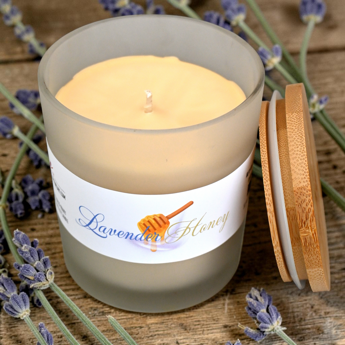 Candle in a glass jar with a wooden lid, surrounded by lavender flowers on a wooden surface.