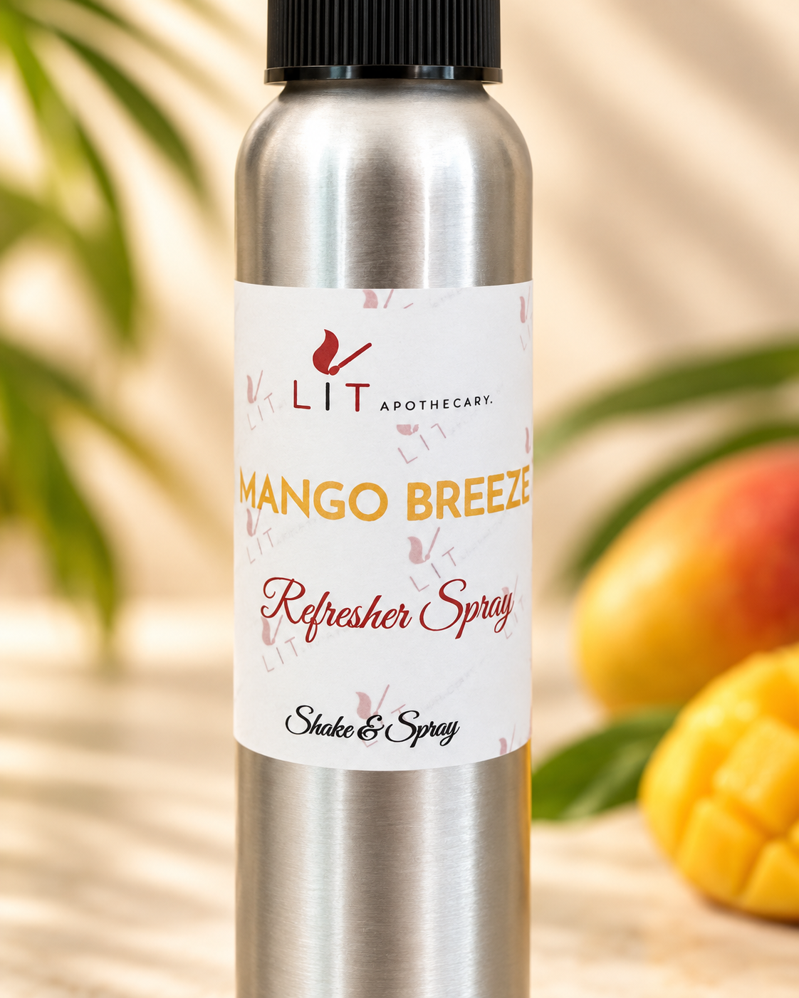 A silver aluminum spray bottle of LIT Apothecary Mango Breeze Refresher Spray, featuring a white label with yellow and red text, set against a warm, blurred background with mangoes and leaves.