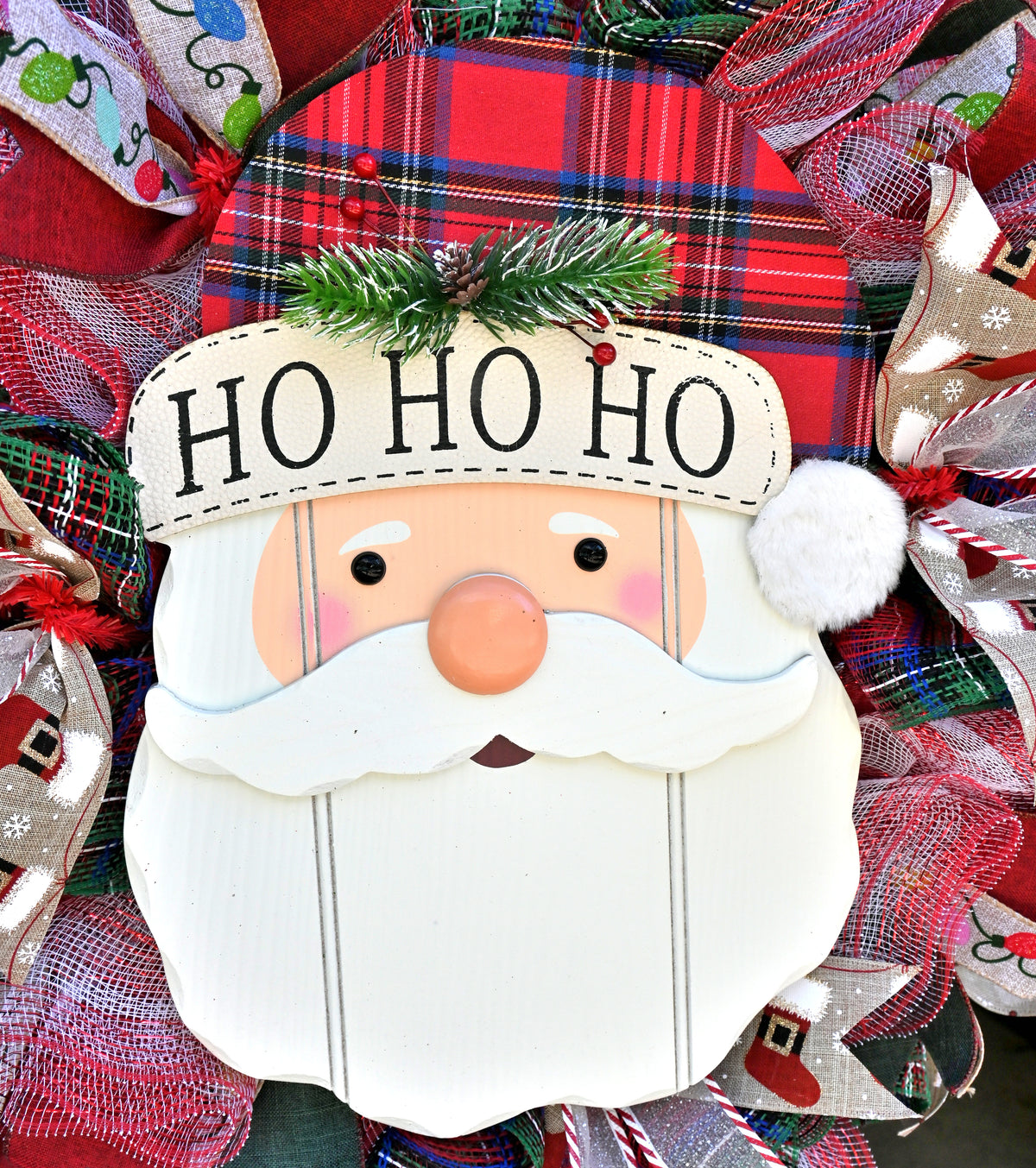 Close-up of the Ho Ho Ho Santa sign on a Christmas wreath with festive red, green, white and plaid accents.