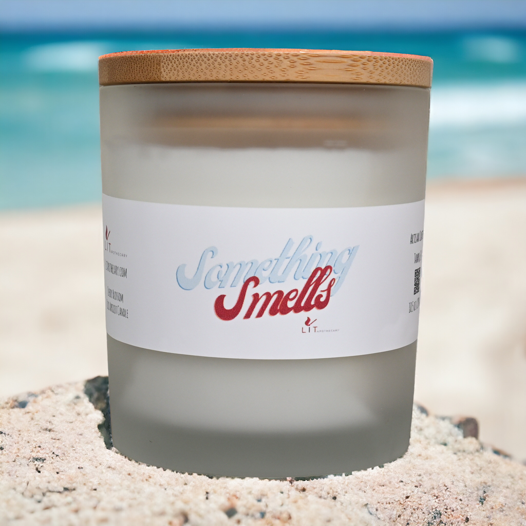 Something Smells cherry blossom candle in frosted glass with bamboo lid and white label on a sandy beach setting