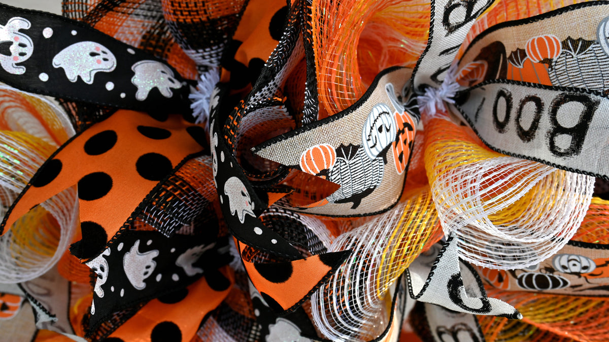 Close-up of Halloween wreath ribbons with orange dots, burlap, glitter ghosts and Boo designs for festive front door decor.