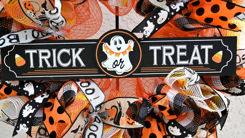 Close-up of Trick or Treat ghost sign on a colorful Halloween wreath with orange, black, yellow and white accents.