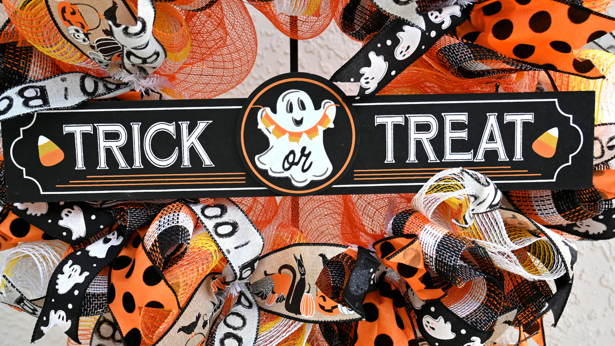 Close-up of Trick or Treat ghost sign on a colorful Halloween wreath with orange, black, yellow and white accents.