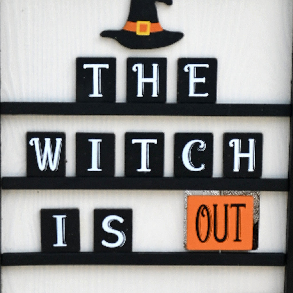 Witch Is Out side of reversible Halloween wreath sign with orange, black and white decor.