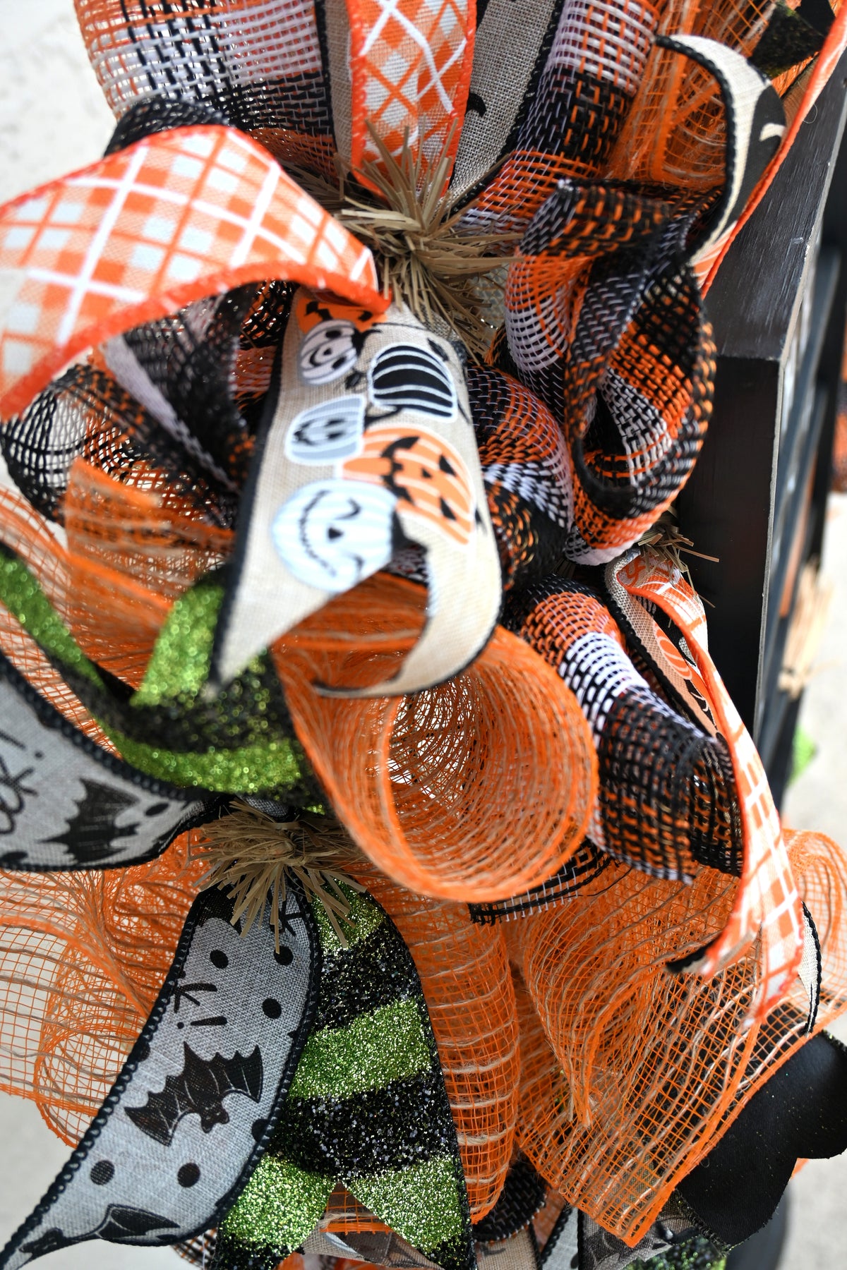 Close-up of Halloween witch wreath ribbons with cats, pumpkins, bats, glitter and plaid patterns.