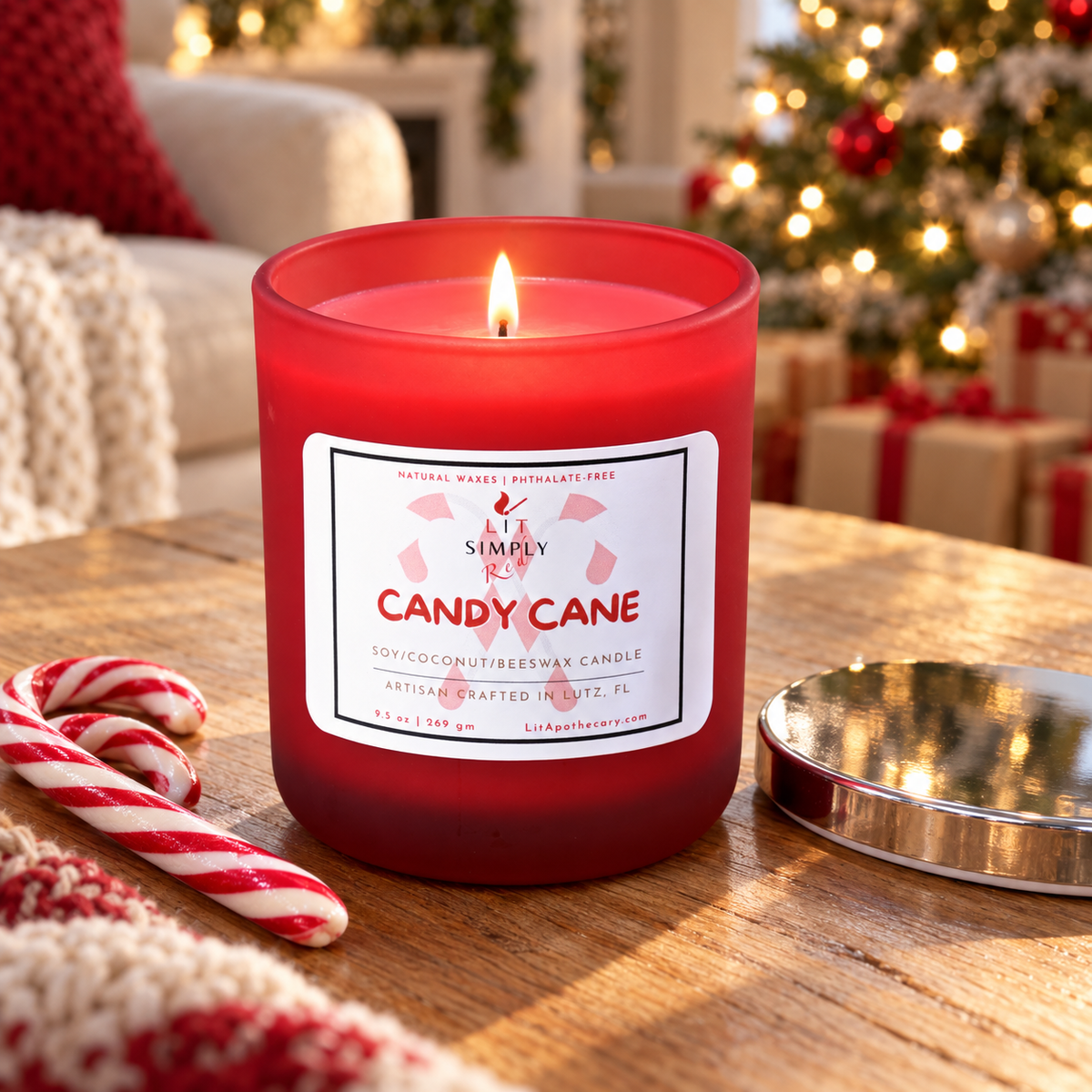 Lit Candy Cane candle burning on a wood coffee table beside peppermint candy canes, with a Christmas tree glowing in the background.