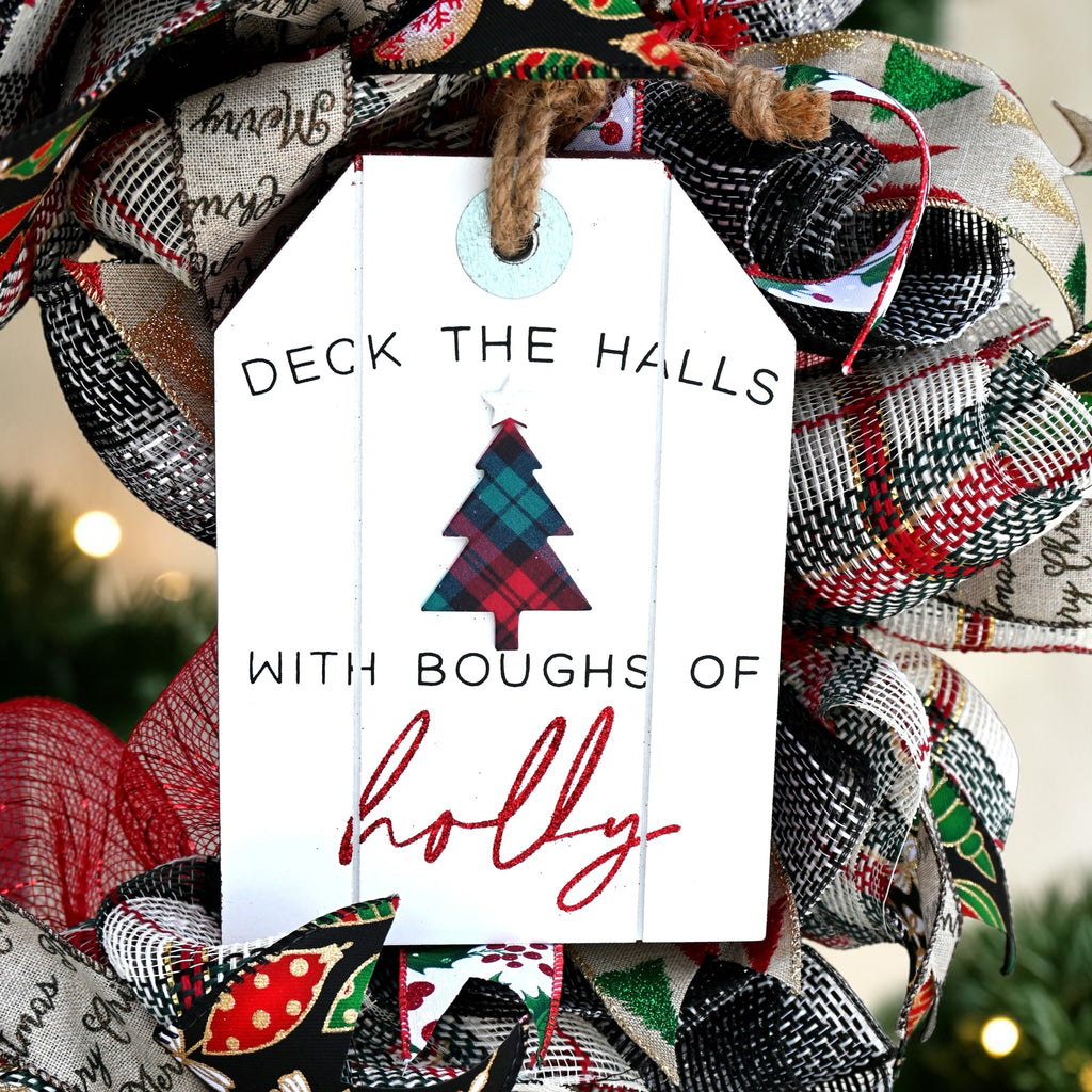 Close-up of the white Deck the Halls with Boughs of Holly sign with a plaid Christmas tree