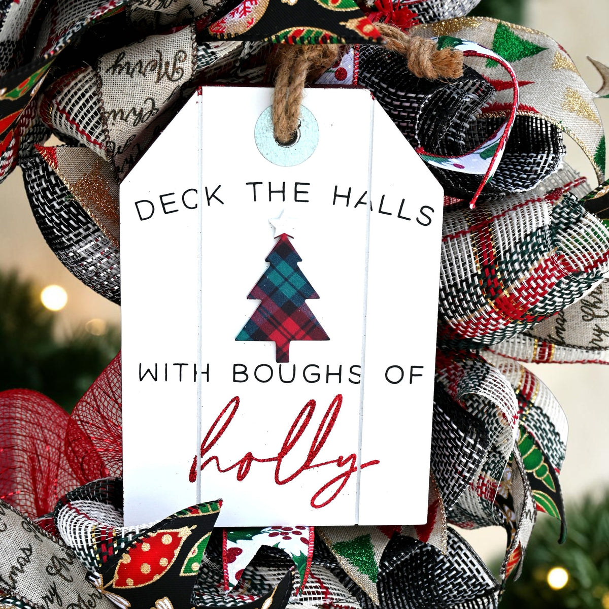 Close-up of the white Deck the Halls with Boughs of Holly sign with a plaid Christmas tree