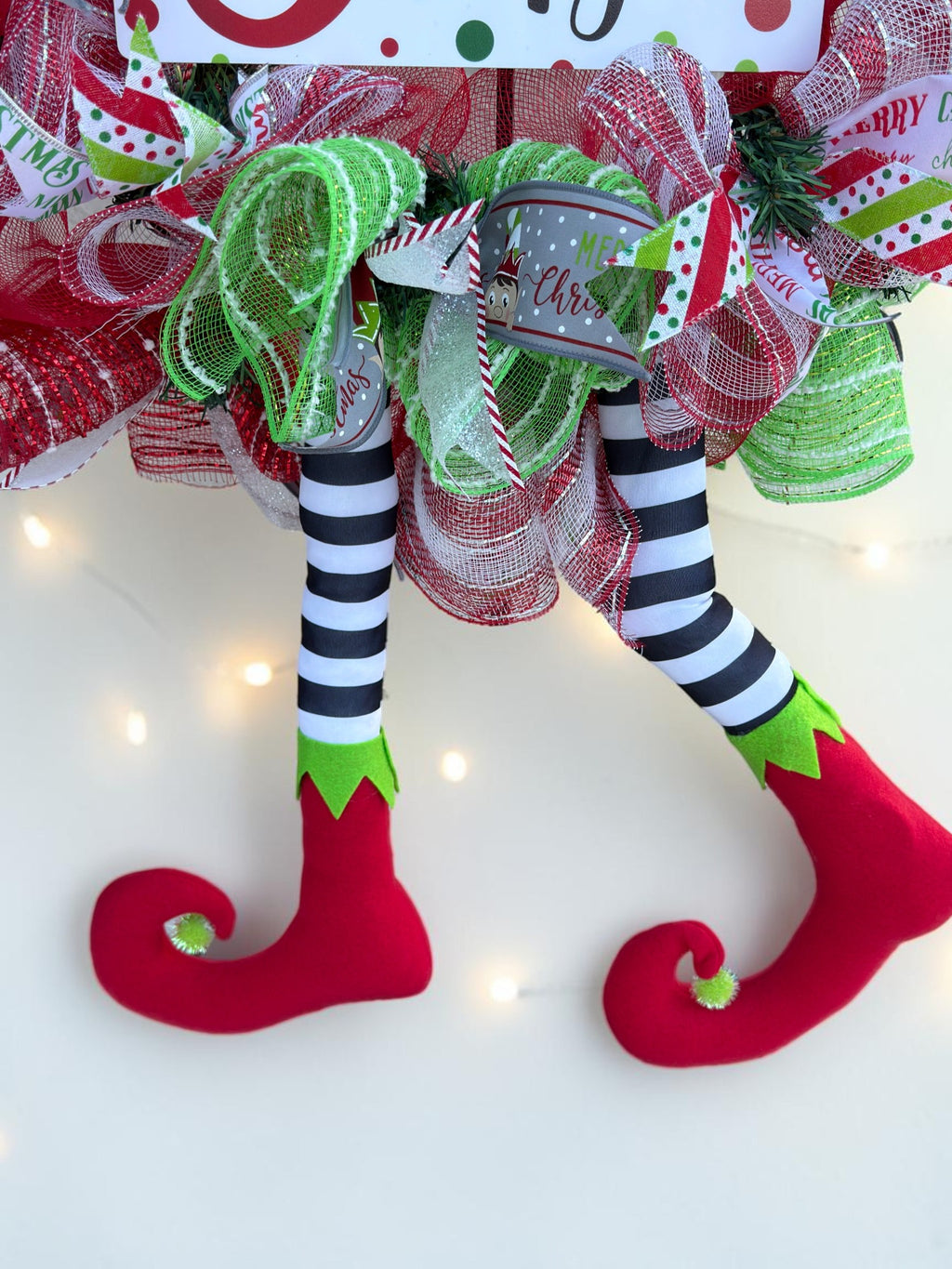 Black and white striped elf legs with curled red boots and lime green cuffs on Christmas wreath.