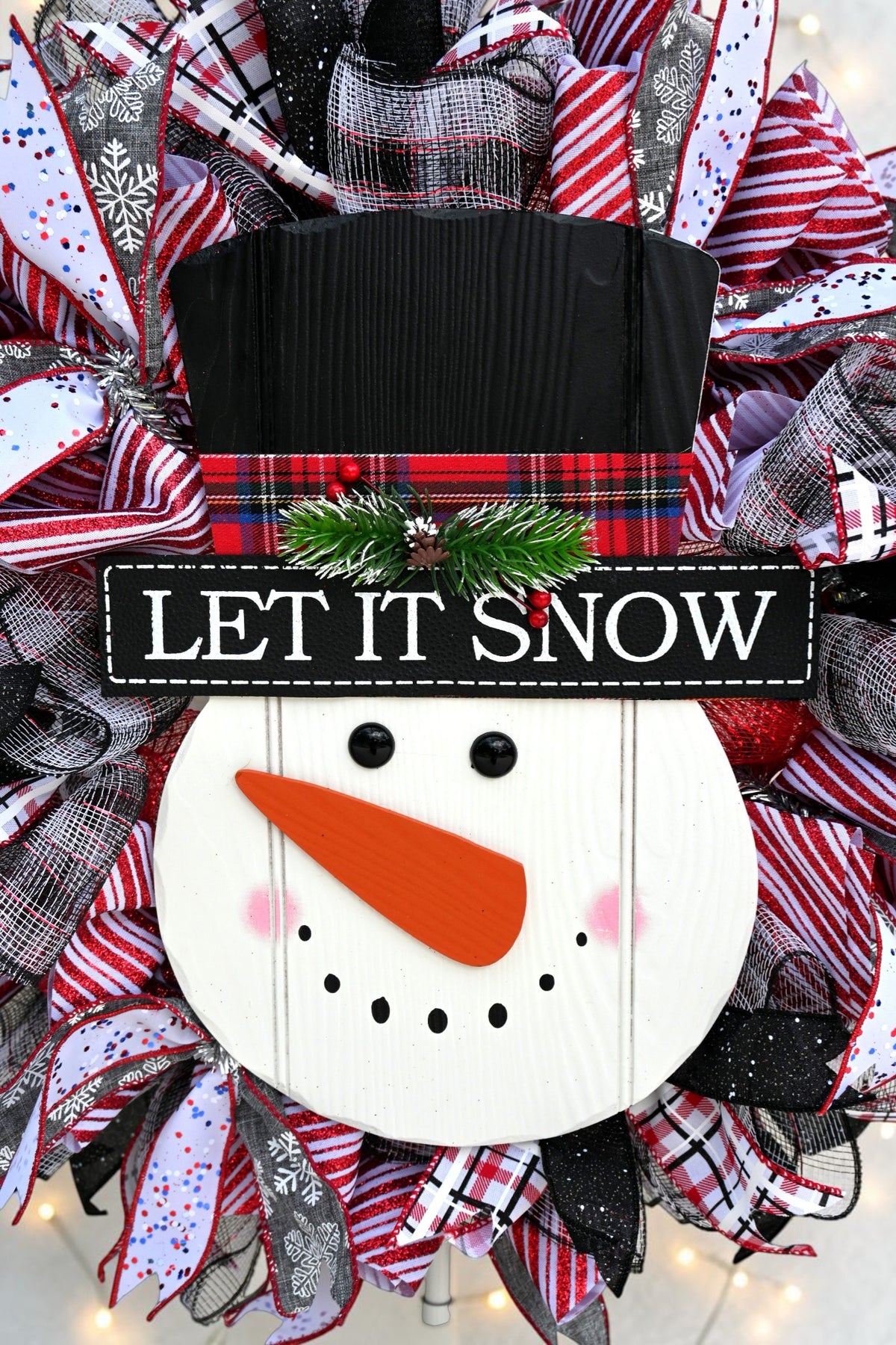 Wooden snowman face with carrot nose, black top hat and Let It Snow sign on Christmas wreath
