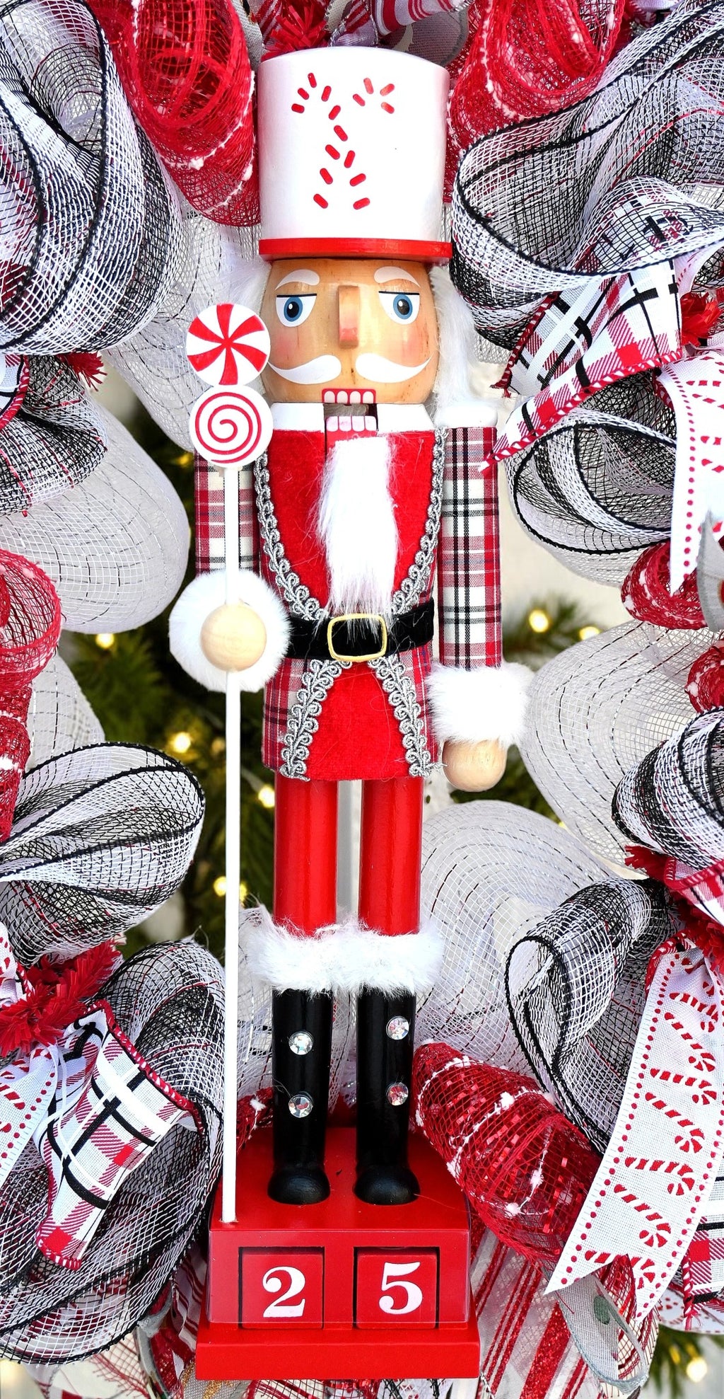 Red nutcracker centerpiece with a white candy cane hat, peppermint staff, plaid sleeves, black boots and Christmas countdown blocks.