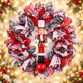 Red, white and black Nutcracker Christmas wreath with peppermint ribbons and a red nutcracker centerpiece against festive golden lights.