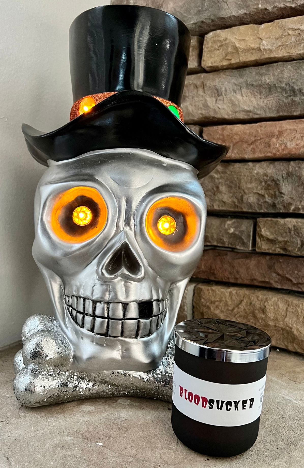 Closed Bloodsucker candle with silver lid beside an illuminated skull and crossbones Halloween decoration