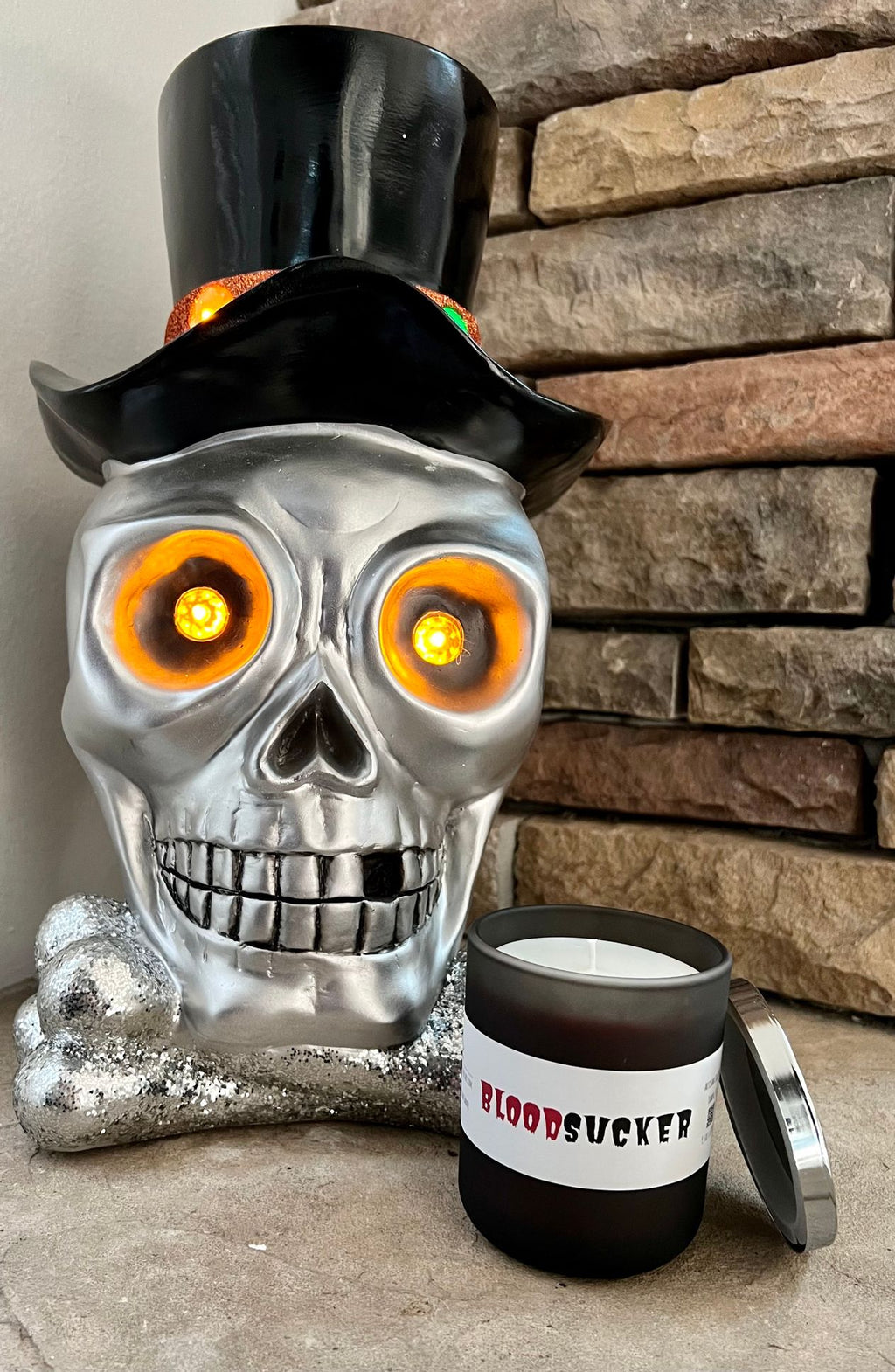 Open Bloodsucker candle beside a silver skull wearing a black top hat, displayed against a stone fireplace