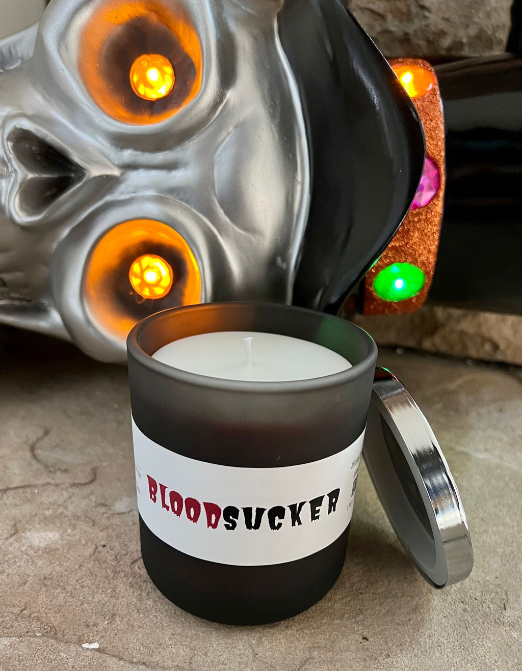 Open Bloodsucker candle with white wax and a single wick, silver lid leaning against the black jar