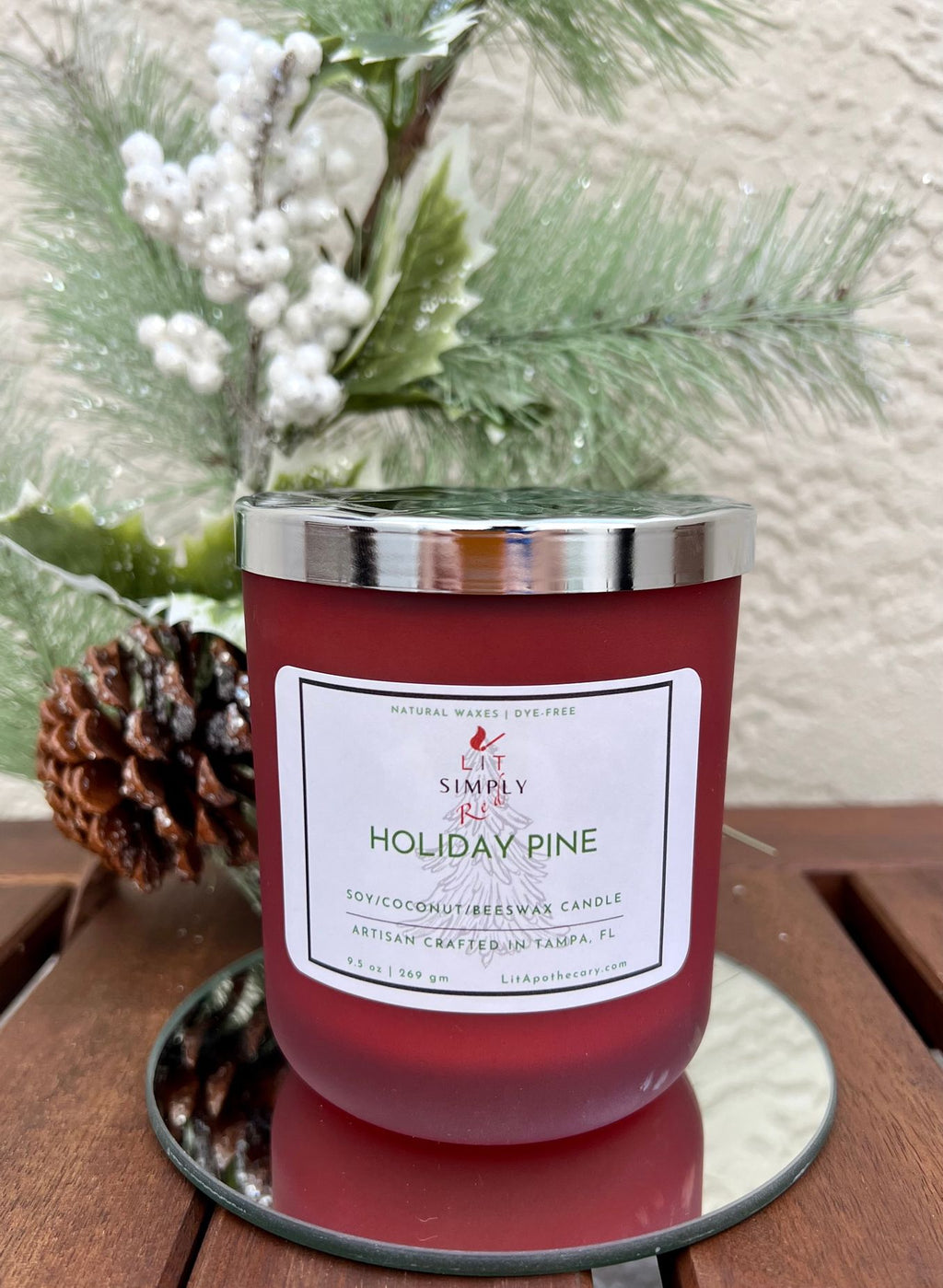 Holiday Pine candle with silver lid on a mirrored tray, with frosted greenery, white berries and a pinecone behind it