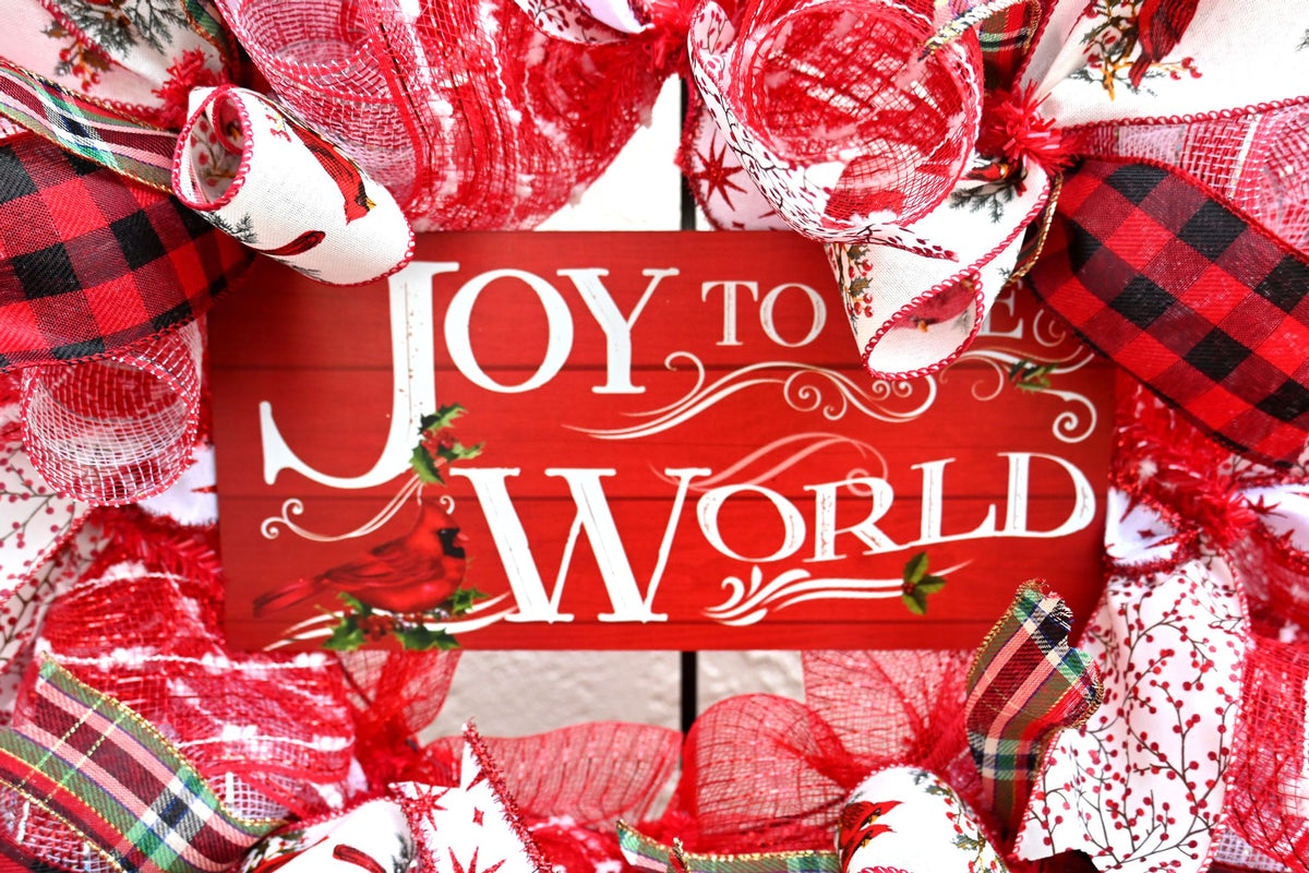 Joy to the World cardinal sign detail on a festive Christmas wreath with layered holiday ribbons.