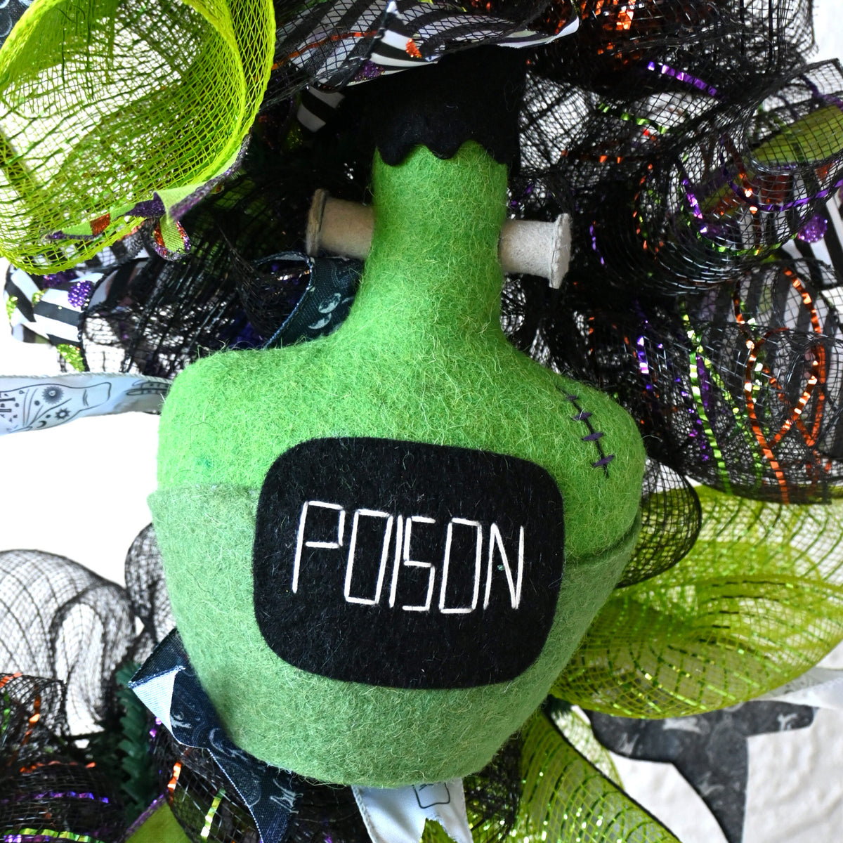 Close-up of poison bottle centerpiece on a Hocus Pocus Halloween wreath with witchy apothecary ribbons and bright seasonal colors.