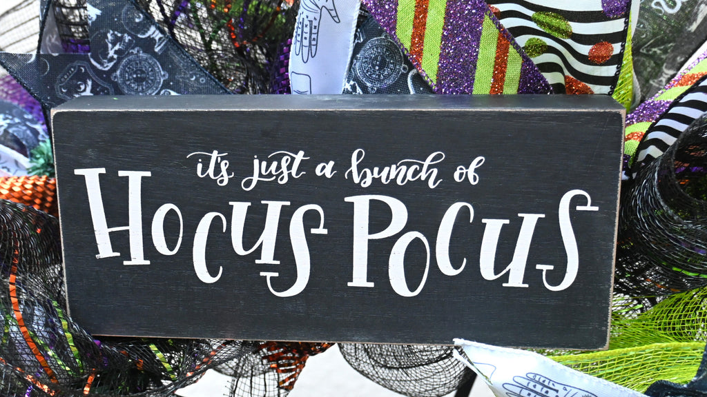 Close-up of It’s just a bunch of Hocus Pocus sign on a poison bottle Halloween wreath with purple, green, orange and black accents.