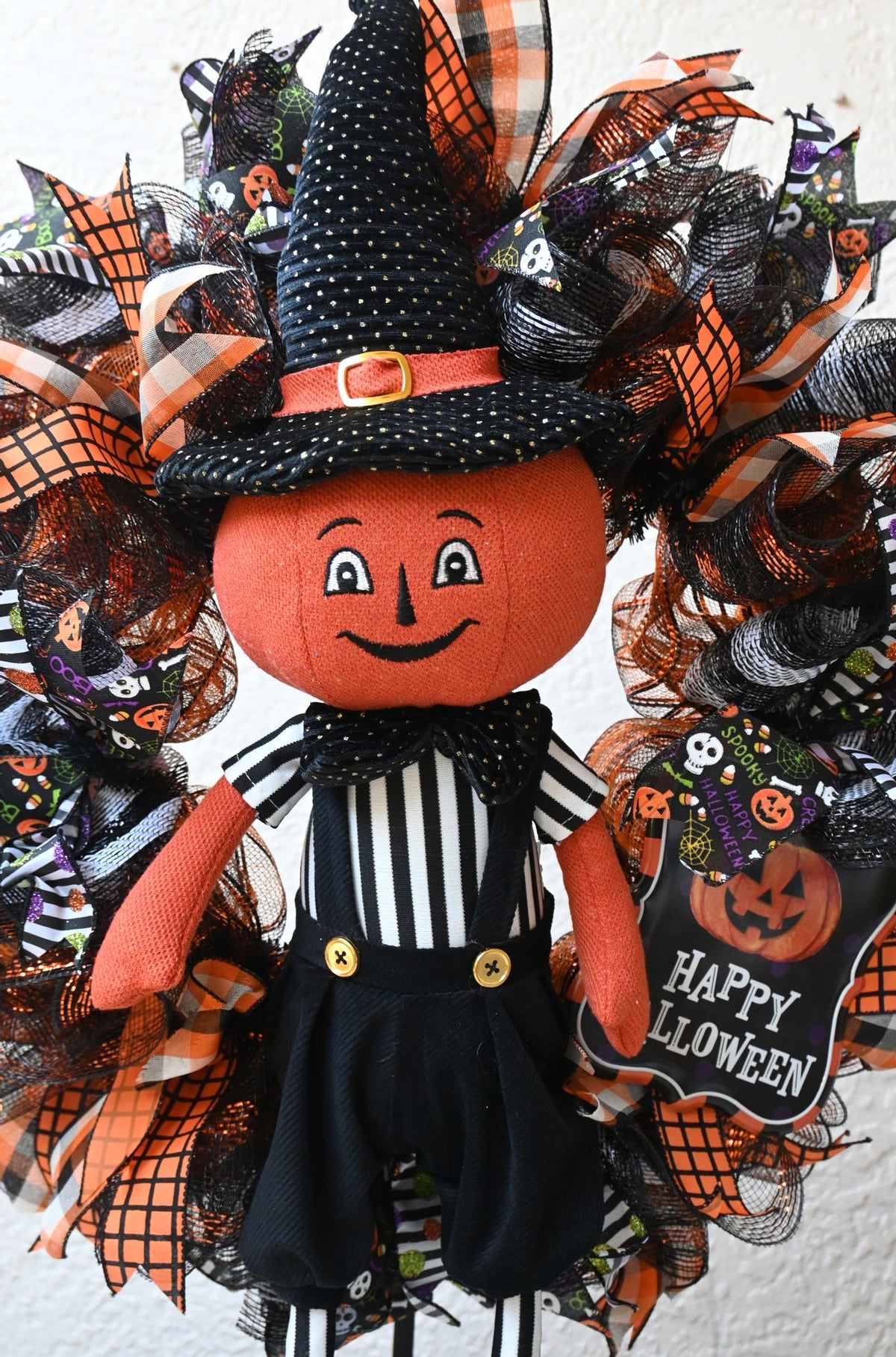 Close-up of pumpkinhead figure on a Halloween wreath with orange, black and white seasonal accents.