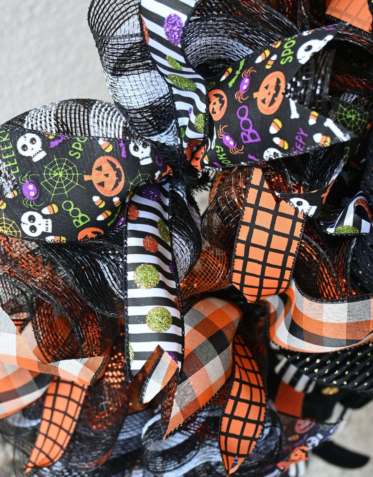 Close-up of Halloween pumpkin wreath ribbons with plaid, stripes, glitter dots and spooky seasonal character details.