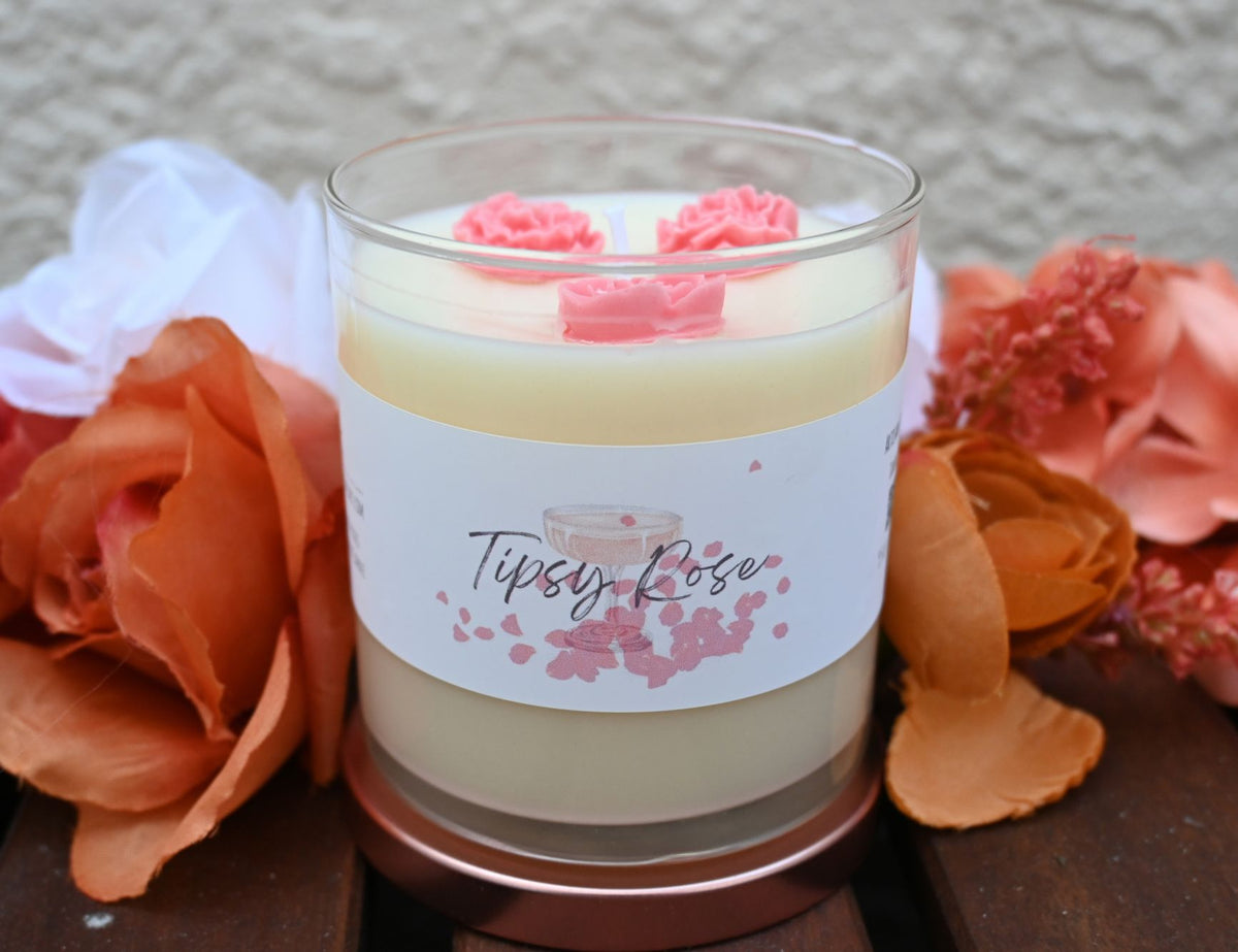 Open Tipsy Rose wine and roses candle in clear glass jar with pink rose wax accents among silk flowers