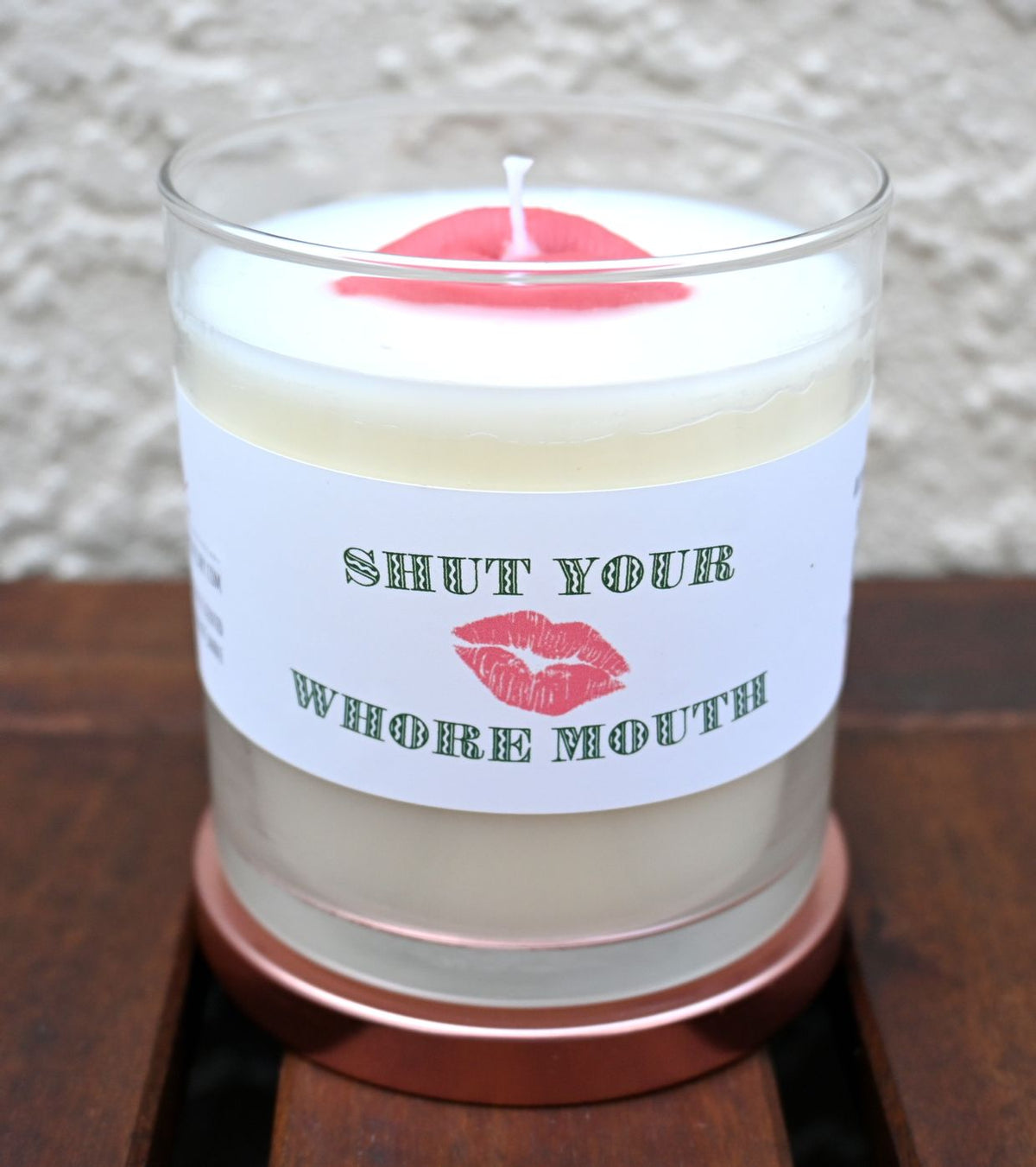 Front view of open Shut Your Whore Mouth candle with red lips on white wax